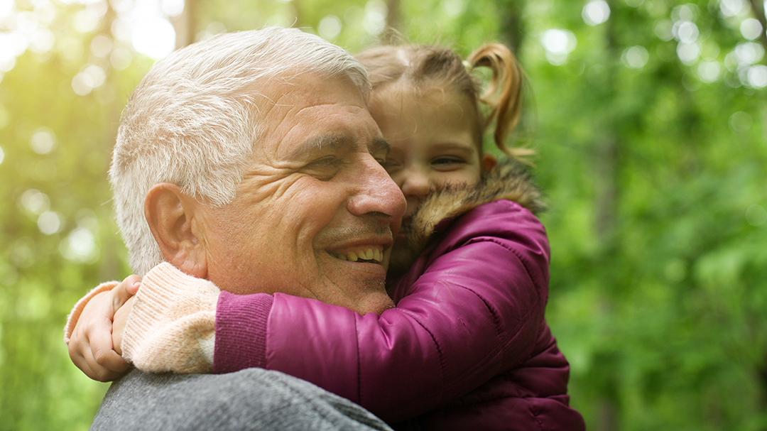 Vanhahko mies ja lapsi halaavat, taustalla vihreää luontoa