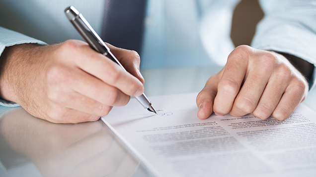 Kuvassa henkilön kädet allekirjoittamassa kynällä asiakirjaa.